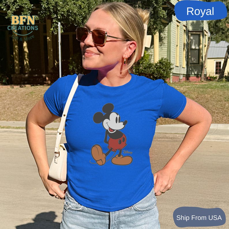 May include: Royal blue t-shirt featuring a classic Mickey Mouse graphic. The cartoon character is depicted in his iconic red shorts, yellow shoes, and white gloves. The shirt has short sleeves and a crew neck. The image also includes the text "BFN Creations & More".