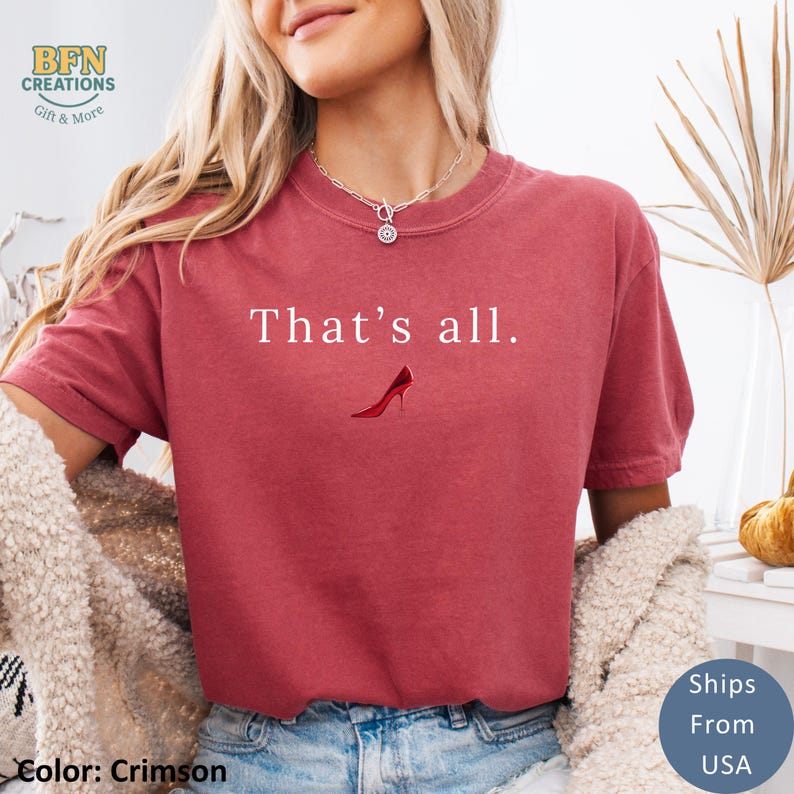 May include: Crimson-colored t-shirt with the text "That's all." and a red high-heeled shoe graphic. The shirt is a solid color and has a crew neck. The shirt is a casual style.