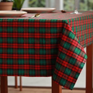 Puede incluir: Un mantel a cuadros rojo, verde y negro cubre una mesa de madera. El mantel presenta un diseño de tartán clásico, con líneas que se cruzan formando una cuadrícula de cuadrados. Los colores son vibrantes y la tela parece ser de peso medio.