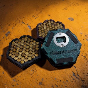 Könnte beinhalten: Drei Flaschenöffner und Munitionshalter auf einer orangefarbenen Oberfläche. Ein Flaschenöffner ist teal mit einem silbernen Öffner und dem Text "slingerstore.com". Zwei Halter sind schwarz und lila, gefüllt mit messingfarbenen Kugeln.