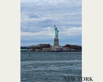 May include: The Statue of Liberty stands tall in New York Harbor under a cloudy sky. The image includes the text "NEW YORK" at the bottom, with the statue's green color contrasting against the water.