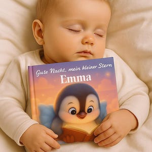 May include: A sleeping baby wearing a white long-sleeved shirt, holding a children's book. The book cover features a cartoon penguin reading a book, with the text "Gute Nacht, mein kleiner Stern Emma". The background is a soft, warm color.