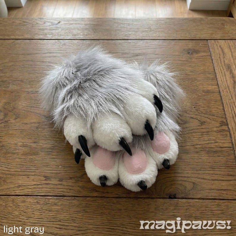 Puede incluir: Guantes de pata de color gris claro con garras negras y almohadillas rosas. Los guantes est&aacute;n hechos de un material suave y afelpado. El texto "light gray" y "magipaws" son visibles.