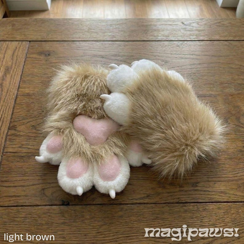 Puede incluir: Guantes de pata de color marr&oacute;n claro con garras blancas y almohadillas rosas. Los guantes est&aacute;n hechos de un material suave y afelpado y est&aacute;n dise&ntilde;ados para parecerse a las patas de los animales. El texto "magipaws!" est&aacute; en la esquina inferior derecha.