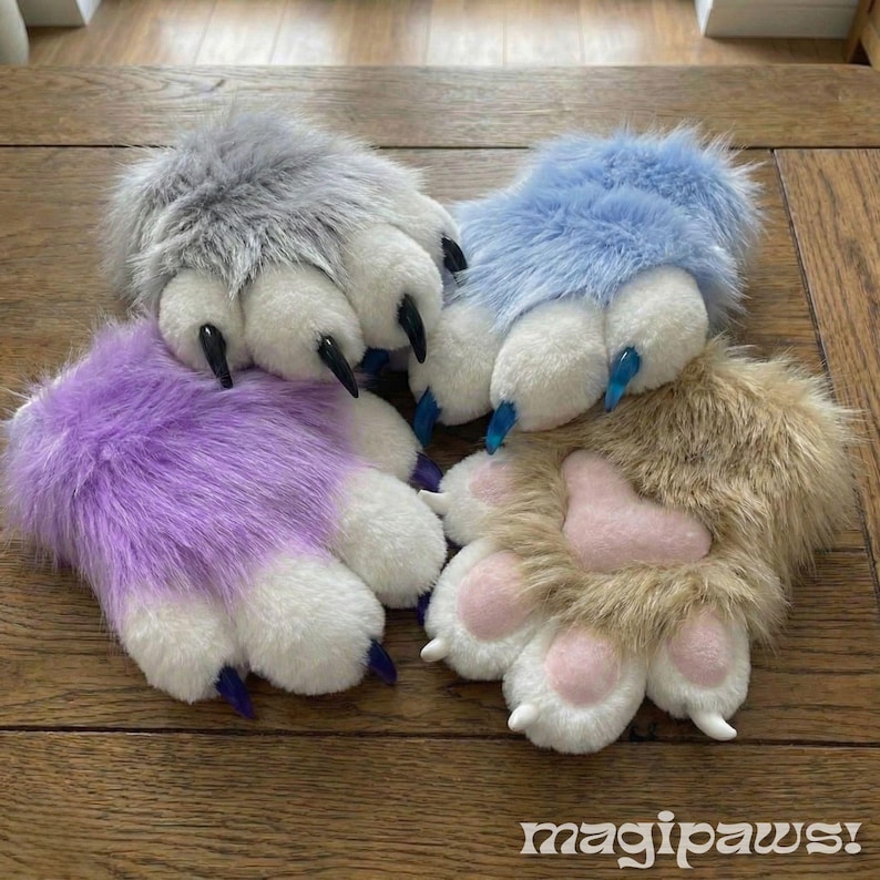 Puede incluir: Cuatro guantes de felpa con forma de pata en gris, azul, morado y beige. Cada pata presenta almohadillas y garras blancas, con acentos rosas en las patas moradas y beige. El logotipo "magipaws!" es visible en la parte inferior.