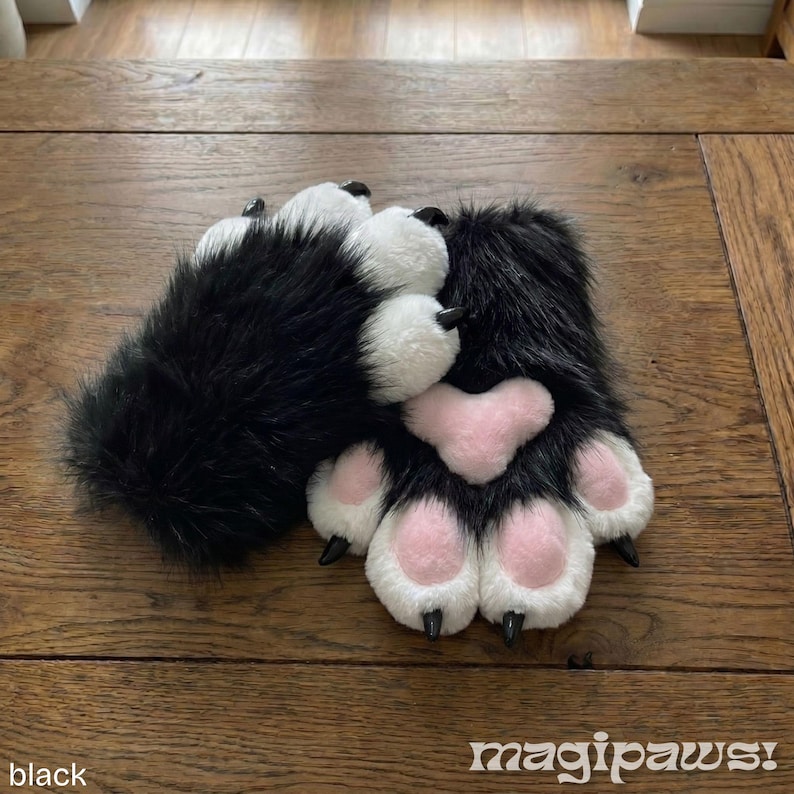 Puede incluir: Un par de guantes de pata peludos en blanco y negro con almohadillas rosas y garras negras. Los guantes est&aacute;n sobre una superficie de madera. El texto "magipaws!" est&aacute; en la esquina inferior derecha.