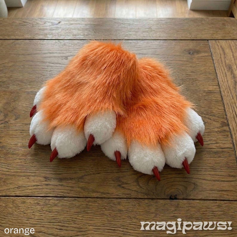 Puede incluir: Patas de piel sint&eacute;tica naranja con almohadillas blancas y garras rojas. Las patas est&aacute;n sobre una superficie de madera. La palabra "orange" est&aacute; en la esquina inferior izquierda, y el texto "magipaws!" est&aacute; en la parte inferior derecha.
