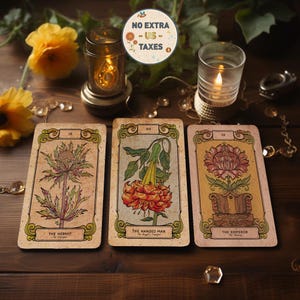 Può includere: Tre carte dei tarocchi con illustrazioni botaniche e bordi ornati sono esposte su una superficie di legno. Le carte sono etichettate come "L'Eremita", "L'Appeso" e "L'Imperatore". L'immagine include anche candele accese, fiori e il testo "NO EXTRA - US - TAXES."