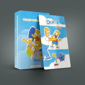 Peut inclure: Un coffret et une carte bleu clair avec des personnages des Simpson. La boîte porte l'inscription "THE SIMPSONS" et des illustrations de Marge, Lisa et Homer Simpson. La carte montre Homer et Bart avec le mot "DEATH".