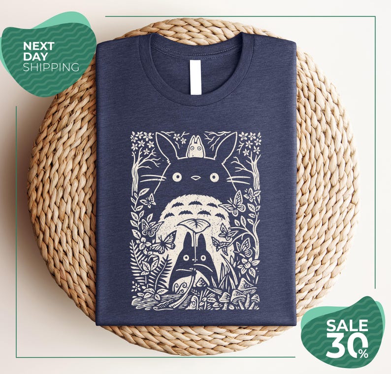 a blue t-shirt with a white graphic design depicting a cat surrounded by various natural elements, such as leaves, flowers, and mushrooms. The t-shirt is placed on a woven placemat, and there are two green circular signs in the image. One sign advertises "Next Day Shipping" and the other sign advertises a "SALE 30%".