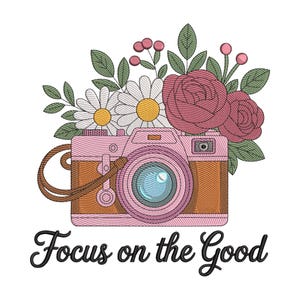 May include: Embroidered design featuring a pink and brown camera with a blue lens, adorned with flowers and leaves. The text "Focus on the Good" is written in a cursive font below the camera.