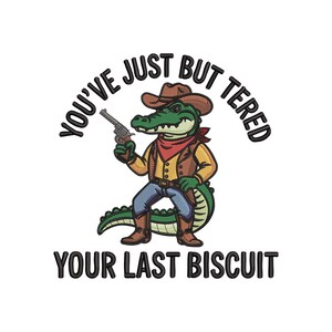 May include: Embroidered design featuring a green alligator dressed as a cowboy, holding a gun. The alligator wears a brown hat, vest, and boots, with a red bandana. Text reads "You've Just Buttered Your Last Biscuit."
