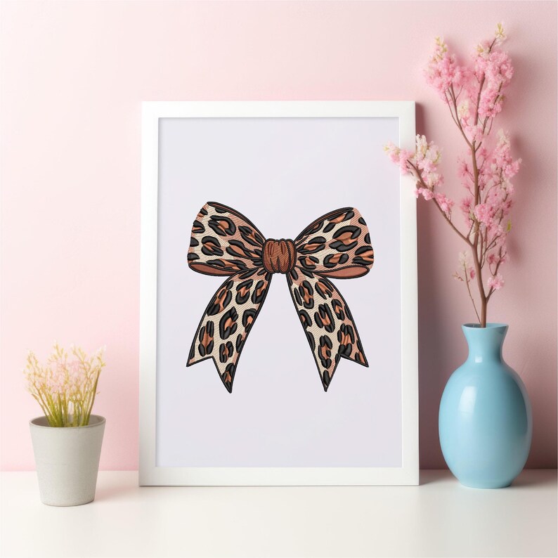 May include: A framed print featuring a decorative bow with a leopard print pattern in shades of brown and black. The bow is centered on a white background, framed in a white border.
