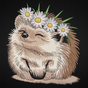 以下が含まれることがあります： デイジーの花冠をかぶった、笑顔のハリネズミの刺繍画像。ハリネズミは茶色とタン色の毛皮で、黒い鼻と閉じられた目があります。デイジーは白い花びらと黄色の中心を持っています。