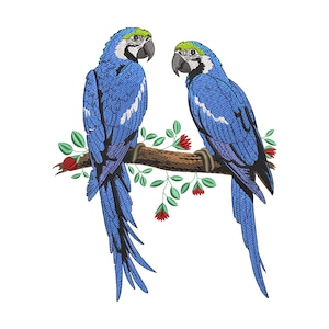 May include: Two embroidered blue macaws perched on a brown branch with green leaves and red flowers. The birds have black beaks, white faces, and yellow and green accents on their heads. The image is set against a white background.