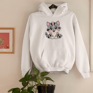 May include: White hooded sweatshirt featuring a colorful embroidered cartoon cat. The cat has gray, pink, and peach fur, with black paws and a smiling expression. The sweatshirt has a front pocket and a drawstring hood.