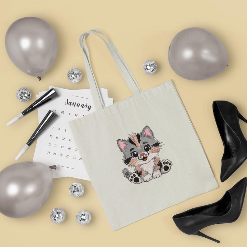 May include: A cream-colored tote bag featuring an embroidered cartoon kitten with gray, pink, and brown fur. The bag is surrounded by silver balloons, disco balls, a calendar page, and black high heels.
