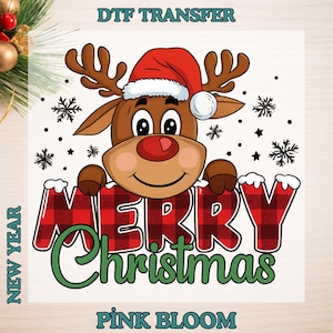 May include: A cartoon reindeer wearing a Santa hat and holding a sign that says "MERRY Christmas" in red plaid letters. The image includes snowflakes and the text "DTF TRANSFER", "NEW YEAR", and "PINK BLOOM".