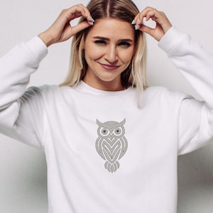 Op de afbeelding: Witte sweatshirt met een gedetailleerd grijs uilontwerp op de voorkant. De uil is gestileerd met ingewikkelde patronen, waardoor hij een textuur krijgt. De sweatshirt heeft lange mouwen en een ronde hals.