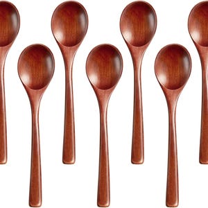 May include: Seven wooden spoons with a rich, reddish-brown finish are arranged against a white background. Each spoon has a rounded bowl and a long, slender handle. The spoons are evenly spaced, showcasing their simple, elegant design.