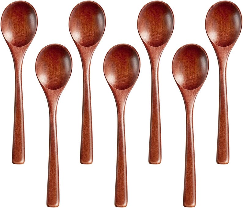 May include: Seven wooden spoons with a rich, reddish-brown finish are arranged against a white background. Each spoon has a rounded bowl and a long, slender handle. The spoons are evenly spaced, showcasing their simple, elegant design.