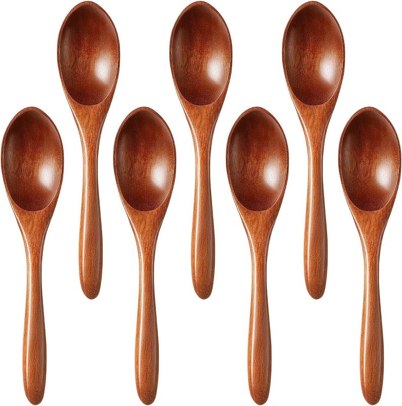 May include: Seven wooden spoons with a rich, warm brown color. The spoons have a classic oval bowl shape and long, slender handles. The spoons are arranged in a symmetrical pattern, showcasing their natural wood grain.