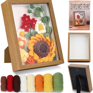 K&ouml;nnte beinhalten: Ein Holzrahmen mit einem Kunstwerk, das eine geh&auml;kelte Sonnenblume und andere Blumen in Gelb, Orange, Rot und Wei&szlig; zeigt. Der hellbraune Rahmen hat einen St&auml;nder. Garngarn in verschiedenen Farben befinden sich unten.