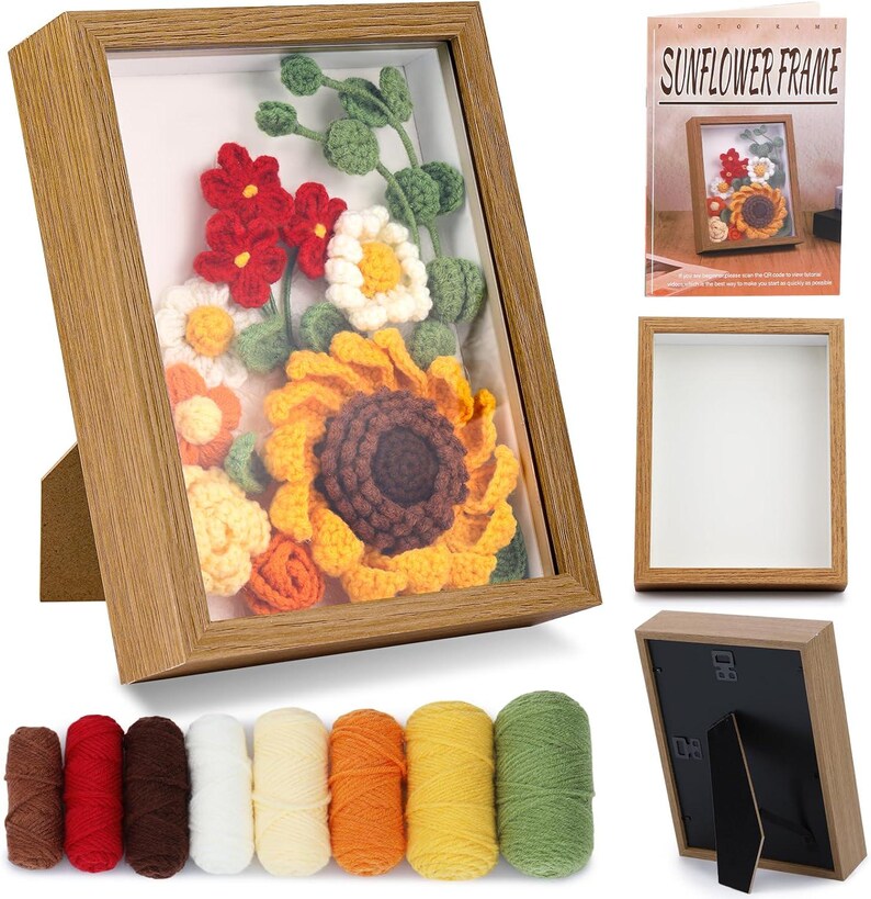 K&ouml;nnte beinhalten: Ein Holzrahmen mit einem Kunstwerk, das eine geh&auml;kelte Sonnenblume und andere Blumen in Gelb, Orange, Rot und Wei&szlig; zeigt. Der hellbraune Rahmen hat einen St&auml;nder. Garngarn in verschiedenen Farben befinden sich unten.