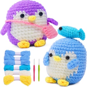 K&ouml;nnte beinhalten: Zwei geh&auml;kelte Pinguin-Spielzeuge, eines lila und eines blau, mit wei&szlig;en B&auml;uchen, gelben F&uuml;&szlig;en und schwarzen Augen. Der lila Pinguin hat einen rosa Schal und eine rosa Tasche. Ebenfalls enthalten sind blaue, wei&szlig;e und gelbe Garnkn&auml;uel und H&auml;kelnadeln.