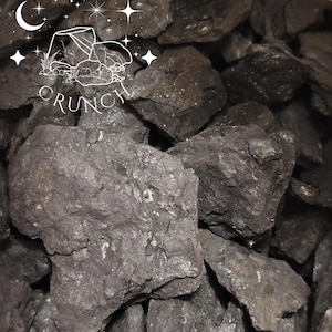 Könnte beinhalten: Ein Haufen dunkelgrauer, grob strukturierter Steine. Die Steine sind unregelmäßig geformt und unterschiedlich groß. Das Bild enthält den Text "EARTHY CRUNCH" mit einer Halbmond- und Sterne-Grafik.