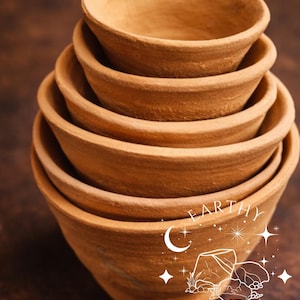 May include: A stack of small, unglazed terracotta pots. The pots are a warm, earthy brown color and have a simple, rounded design. The image includes the text "For Reference Only" and the words "Earthy Crunch".