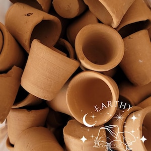 Op de afbeelding: Een verzameling kleine, ongeglazuurde terracotta kleibekers met een matte, aardebruine afwerking. De bekers zijn cilindervormig met open bovenkanten en zichtbare texturen. Een wit grafisch logo met de tekst EARTHY CRUNCH is over de afbeelding geplaatst.