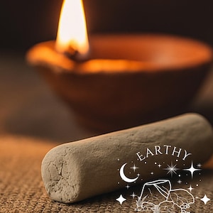 Könnte beinhalten: Eine brennende Öllampe aus Ton mit heller Flamme und ein hellfarbiger, zylindrischer Gegenstand im Vordergrund. Der Gegenstand trägt den Text "EARTHY CRUNCH" mit einem Mond- und Sterndesign. Der Text "For Reference only" ist ebenfalls sichtbar.