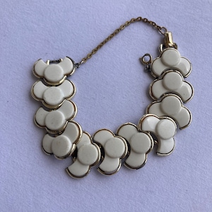 May include: A vintage bracelet featuring white flower-shaped links with gold-tone metal accents. The bracelet has a safety chain and a clasp closure. The floral design adds a touch of retro charm to the jewelry.