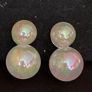 May include: Four iridescent, round, pearl-like beads. Each bead has a pearlescent sheen with hints of pink, green, and yellow. The beads are arranged in two pairs, each pair stacked on top of each other. The background is dark.