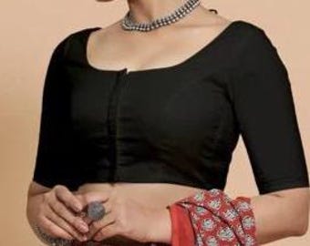 Könnte beinhalten: Eine schwarze Bluse mit kurzen Ärmeln und einem Rundhalsausschnitt. Die Bluse hat einen Frontverschluss und ist mit einem gemusterten rot-weißen Stoff kombiniert. Eine silberne Halskette und ein Ring sind ebenfalls sichtbar.