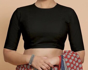 Könnte beinhalten: Eine schwarze Bluse mit kurzen Ärmeln und rundem Ausschnitt. Die Bluse ist aus einem glatten Stoff gefertigt und wird mit einem gemusterten rot-weißen Textil getragen. Die Bluse ist einfarbig und hat ein schlichtes, klassisches Design.