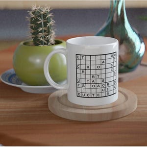 Może przedstawiać: Biały ceramiczny kubek z wzorem krzyżówki. Kubek ma czarną siatkę z literami tworzącymi słowa. Kubek stoi na drewnianej podstawce, z małym kaktusem w zielonej doniczce i dekoracyjnym szklanym wazonem w tle.