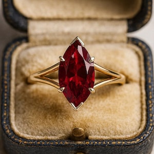Puede incluir: Anillo de oro con un rubí talla marquesa, presentado en un joyero vintage. El rubí es de color rojo intenso y está sujeto por cuatro garras. El anillo tiene un diseño de caña dividida.