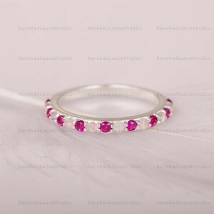 Può includere: Un anello d'argento con pietre preziose rosa e rosa chiaro alternate. L'anello è incastonato con piccole pietre preziose rotonde, creando una fascia continua di colore. Le pietre sono distanziate uniformemente.
