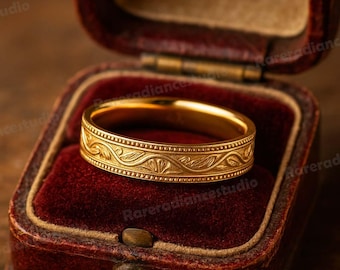 May include: A gold-colored ring with an engraved floral pattern, displayed in a red velvet ring box. The ring has a detailed design around the band. The box is open, revealing the ring's intricate details.