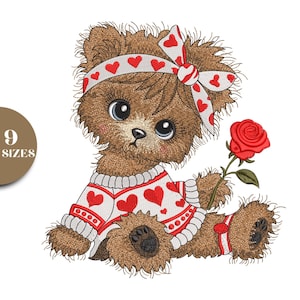 Può includere: Un orsacchiotto ricamato con una rosa rossa. L'orso indossa un maglione bianco con cuori rossi e una fascia e un fiocco abbinati. L'orso ha grandi occhi blu ed è seduto.