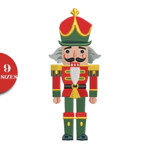 Könnte beinhalten: Gesticktes Bild eines Nussknacker-Soldaten in Rot, Grün und Gold. Der Nussknacker hat einen hohen roten Hut mit goldenen Verzierungen, einen schwarzen Schnurrbart und eine weiße Perücke. Die Uniform des Soldaten ist rot mit goldenen Akzenten und grüner Hose.