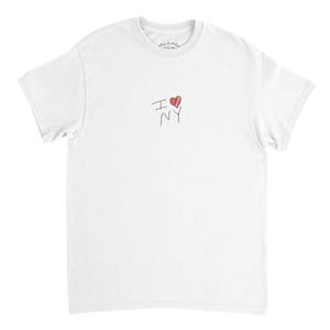 Könnte beinhalten: Weißes T-Shirt mit dem handgeschriebenen Text "I ❤️ NY" in Schwarz und Rot. Das Herz ist rot und die Buchstaben sind in einem einfachen, handschriftlichen Stil gehalten. Das T-Shirt hat einen klassischen Rundhalsausschnitt.