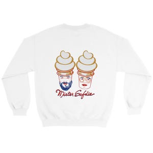 Puede incluir: Sudadera blanca con un diseño lúdico de dos conos de helado con caras, uno con barba y el otro con gafas. El texto rojo en cursiva debajo dice "Mister Safdie".