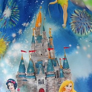 May include: A blue fabric featuring a print of Cinderella's castle, Tinkerbell, and fireworks. The castle is light grey with blue and green accents. Tinkerbell is flying with her fairy dust. The fireworks are colourful and bursting in the sky.