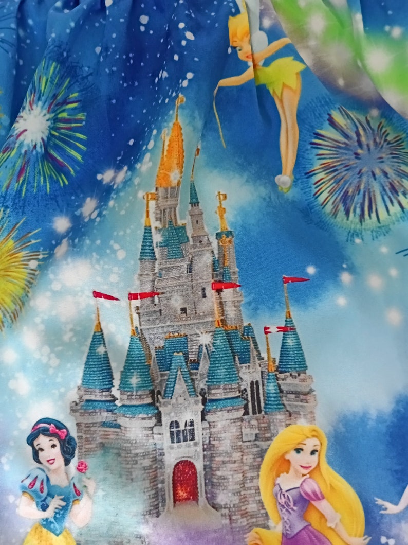 May include: A blue fabric featuring a print of Cinderella's castle, Tinkerbell, and fireworks. The castle is light grey with blue and green accents. Tinkerbell is flying with her fairy dust. The fireworks are colourful and bursting in the sky.