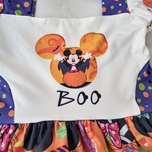 May include: A Halloween dress with a Mickey Mouse design. The white bodice features a Mickey Mouse head graphic in orange and black, with the word "BOO" underneath. The skirt is orange with Halloween patterns.