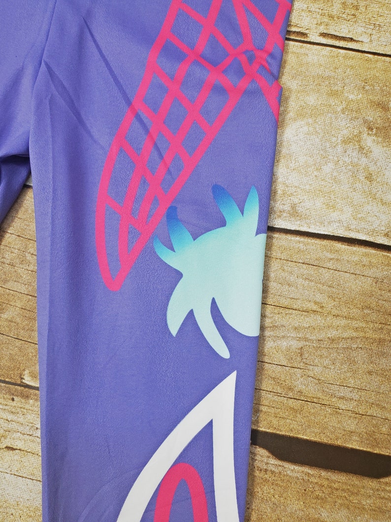 May include: Purple leggings with a pink and white geometric design. The design features a large pink and white geometric shape, a smaller blue and white geometric shape, and a white geometric shape with a pink outline.