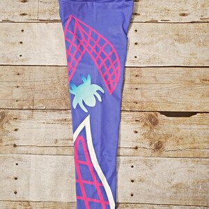 May include: Purple leggings with a pink and white geometric design. The design features a spider web and a stylized spider.